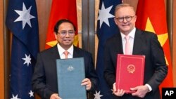 Thủ tướng Việt Nam Phạm Minh Chính (trái) Thủ tướng Úc Anthony Albanese trao đổi tài liệu trong buổi lễ ký kết nâng cấp quan hệ Việt - Úc tại Canberra, ngày 7/3/2024.