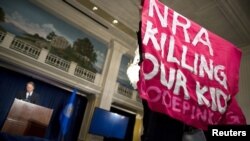 A protester holds up a sign during a speech by Wayne LaPierre (L), Executive Vice President of the National Rifle Association (NRA), during a news conference in Washington December 21, 2012. NRA, the powerful U.S. gun rights lobby, went on the offensive o