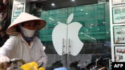 Một người bán rong đi ngang qua một cửa hàng bán sản phẩm của Apple ở Hà Nội. Theo Bloomberg và Business Insider, các công ty của Trung Quốc đang tranh giành công nhân của nhà sản xuất lớn nhất cho Apple ở Việt Nam.