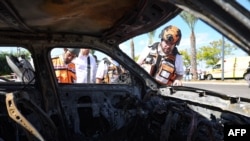 First responders check a charred car near a building hit by a rocket fired from Lebanon in Kiryat Ata in Israel's Haifa district on October 19, 2024, amid the ongoing war between Israel and Hezbollah.