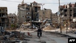 Cư dân lái xe gắn máy ngang qua một tòa nhà bị hư hại ở Harasta, phía đông thủ đô Syria, Damascus, ngày 10/2/2016.