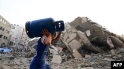 A boy carries a gaz canister as he walks in front of a building that collapse during an Israeli air strike in Gaza City early on October 8, 2023.