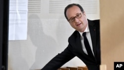 FILE - French president Francois Hollande picks up ballots before voting in the first round of the presidential election in Tulle, central France, Apr. 23, 2017. 